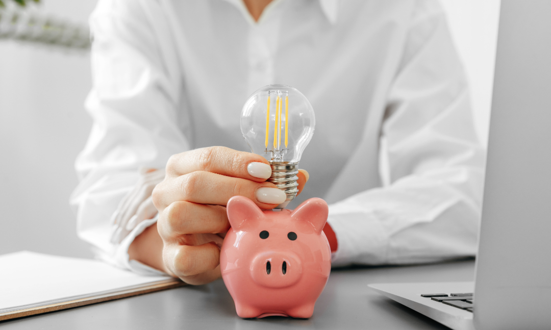  Ja, auch hier sollte ein Alt-Text hin.  Das Bild einer Hand, die eine leuchtende Glühbirne in ein rosa Sparschwein steckt, symbolisiert den Kosten- und Wettbewerbsvorteil von KAN-ONE